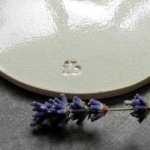 Puede incluir: Plato de cer&aacute;mica blanco con borde redondeado y acabado liso y brillante. El plato tiene una peque&ntilde;a marca en relieve en la parte inferior que dice "#15".