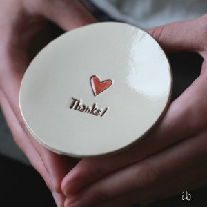 May include: A white ceramic dish with a red heart and the words "Thanks!" in brown lettering.