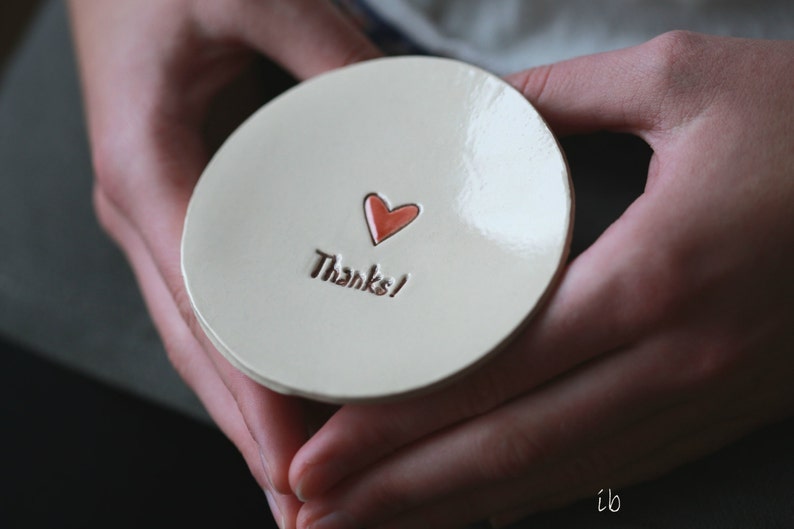 May include: A white ceramic dish with a red heart and the words "Thanks!" in brown lettering.