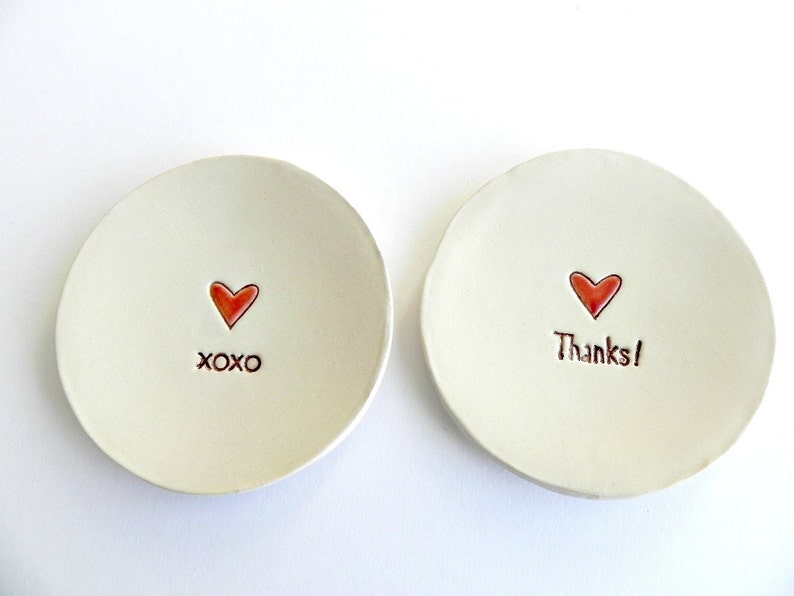 May include: Two small white ceramic dishes with red hearts and handwritten messages. One dish says "XOXO" and the other says "Thanks!"
