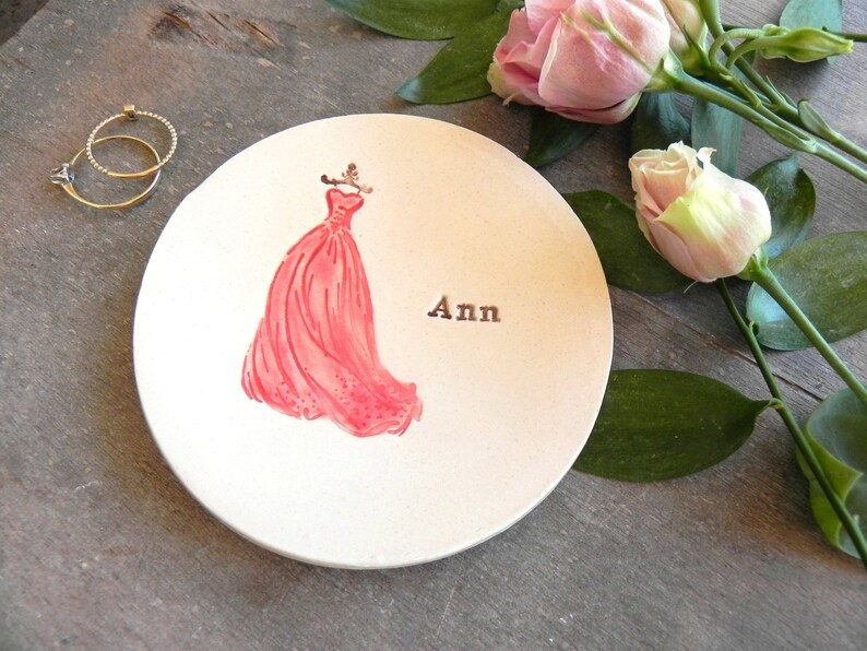 May include: White ceramic ring dish with a pink dress illustration and the name "Ann" written on it.