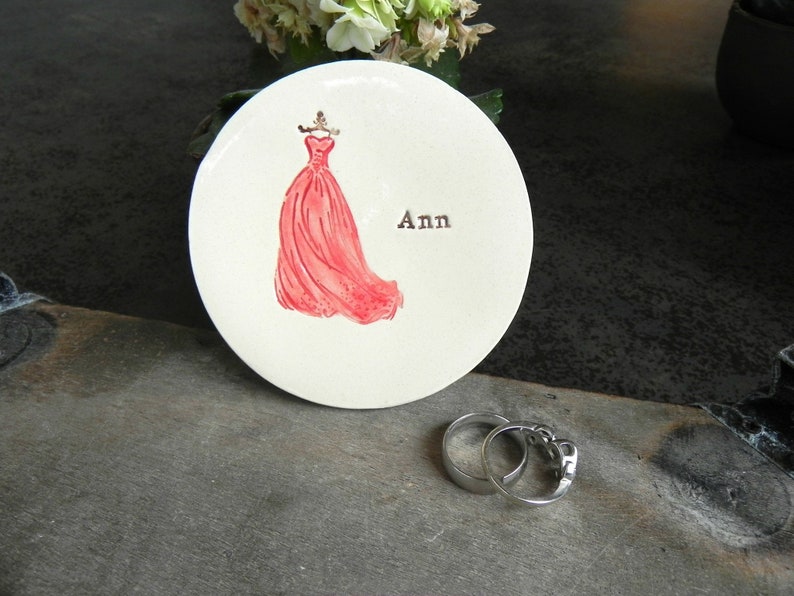 May include: White ceramic ring dish with a pink dress design and the name "Ann" written on it.