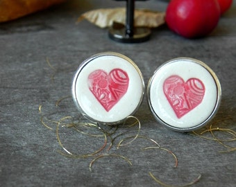 May include: A pair of cufflinks with a white background and a pink heart design. The hearts have a detailed pattern.