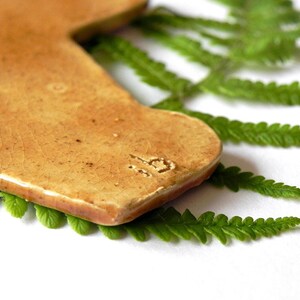 May include: A light brown ceramic tile in the shape of a state of Texas with a brown fern leaf behind it. The tile has a number "19" stamped on it.