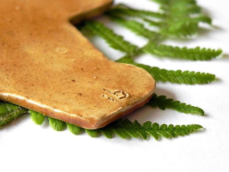 May include: A light brown ceramic tile in the shape of a state of Texas with a brown fern leaf behind it. The tile has a number "19" stamped on it.