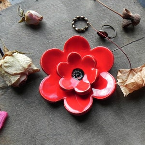 Puede incluir: Un plato de cerámica rojo en forma de flor con un centro negro. El plato tiene forma de flor con cinco pétalos.