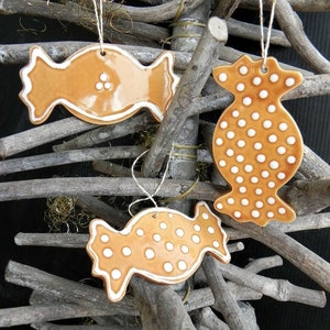 May include: Three brown ceramic ornaments shaped like candy with white polka dots and white outlines hanging on brown twigs.
