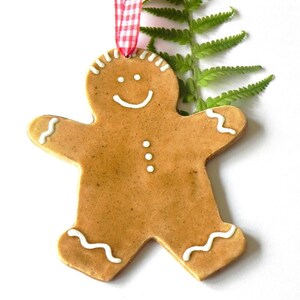 May include: A gingerbread man Christmas ornament with white icing details. The ornament is brown and has a red and white ribbon attached.