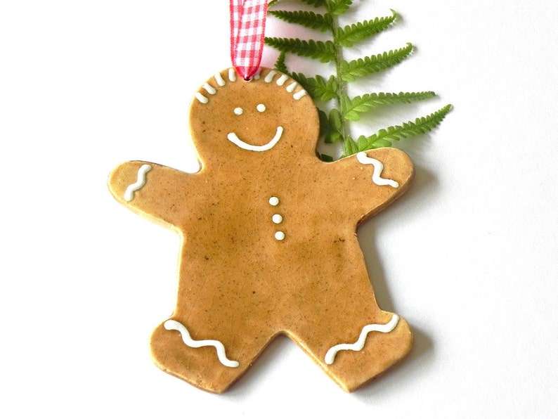 May include: A gingerbread man Christmas ornament with white icing details. The ornament is brown and has a red and white ribbon attached.