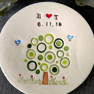 May include: A white ceramic plate with a green tree design made of circles. The tree has a brown trunk and red flowers at the base. The plate also has two blue birds, a red heart, and the text "B &hearts; T 6.11.18".
