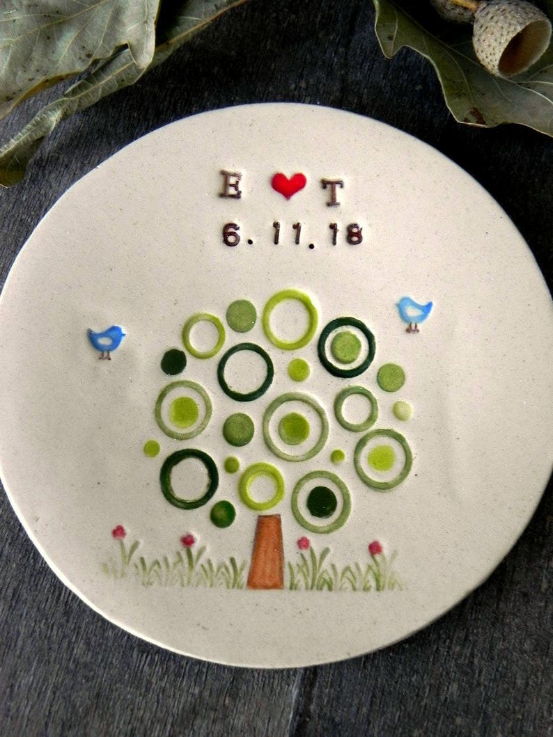 May include: A white ceramic plate with a green tree design made of circles. The tree has a brown trunk and red flowers at the base. The plate also has two blue birds, a red heart, and the text "B &hearts; T 6.11.18".