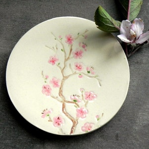 Puede incluir: Un plato de cerámica blanco con un diseño en relieve de una rama de cerezo rosa.