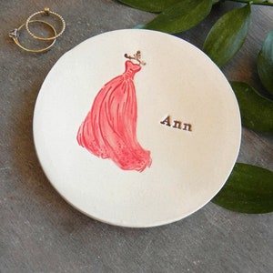May include: White ceramic ring dish with a red dress design and the name "Ann" written on it.