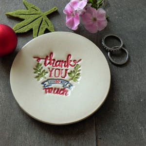 May include: White ceramic ring dish with a red, blue, and green floral design and the text "Thank You So Much".