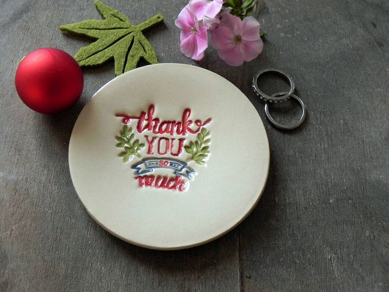 May include: White ceramic ring dish with a red, blue, and green floral design and the text "Thank You So Much".