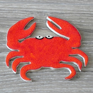 Könnte beinhalten: Eine rote Keramik-Krabbe mit weißen Umrissen und schwarzen Augen. Die Krabbe ist ein Dekorationsobjekt.