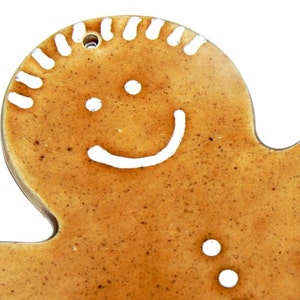 May include: A gingerbread man cookie ornament with a white icing smile and eyes. The cookie is brown and has a speckled texture.