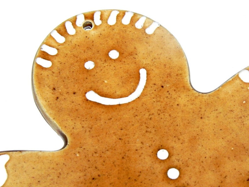 May include: A gingerbread man cookie ornament with a white icing smile and eyes. The cookie is brown and has a speckled texture.