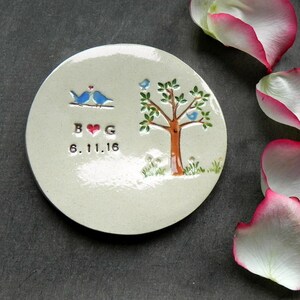 May include: A white ceramic ring dish with a tree and two birds painted on it. The dish also has the letters "B & G" and the date "6.11.16" painted on it.