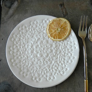 Pode incluir: Prato de cer&acirc;mica branco com um design de renda em relevo. Uma fatia de lim&atilde;o seca est&aacute; no prato.