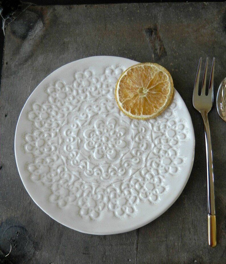 Pode incluir: Prato de cer&acirc;mica branco com um design de renda em relevo. Uma fatia de lim&atilde;o seca est&aacute; no prato.