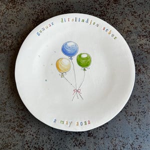 Puede incluir: Un plato de cerámica blanco con un diseño de globos de colores y el texto "Gefeliciteerd" en holandés, "dit" en holandés, "lind" en holandés, "jen" en holandés, "arbor" en holandés y "2 de mayo de 2023" en inglés.