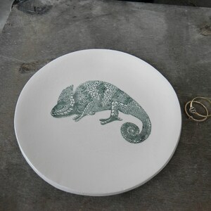 Puede incluir: Un plato de cer&aacute;mica blanco con un dise&ntilde;o de camale&oacute;n verde. El plato es redondo y tiene un borde ligeramente elevado.