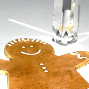 May include: A brown gingerbread man cookie with white icing details, including a smiling face and buttons. The cookie is on a white surface.