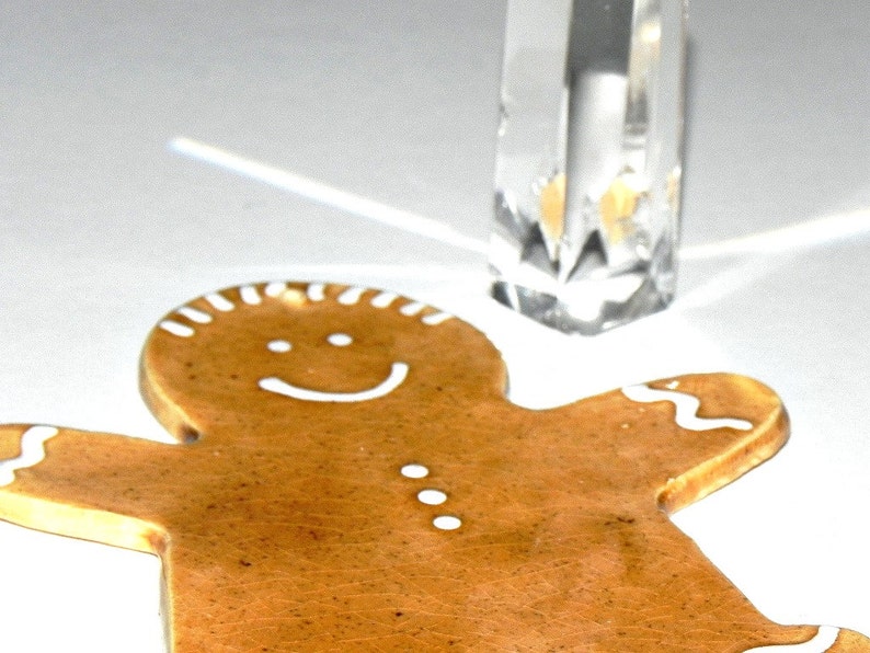 May include: A brown gingerbread man cookie with white icing details, including a smiling face and buttons. The cookie is on a white surface.