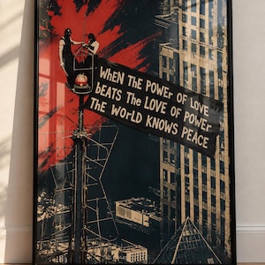 May include: A framed poster featuring a dark, high-contrast graphic of two figures on a tall antenna tower against a red and black background. A banner hangs from the tower with the text: When The Power Of Love Beats The Love Of Power The World Knows Peace.