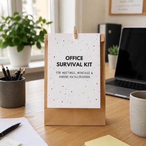 Könnte beinhalten: Eine braune Papiertüte mit einer oben angeklammerten weißen Karte. Die Karte zeigt schwarze Punkte und den Text: OFFICE SURVIVAL KIT FÜR MEETINGS, MONTAGE & ANDERE KATASTROPHEN. Die Tüte steht aufrecht auf einer hölzernen Schreibtischoberfläche.