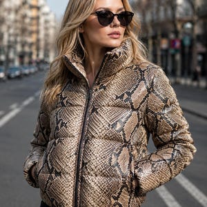 May include: A puffer jacket featuring a brown and black snakeskin print pattern, a high collar, and a central black zip closure. The jacket has long sleeves and two side pockets, constructed with a quilted design throughout the exterior.