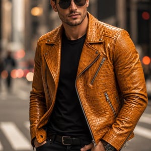 May include: A tan leather motorcycle jacket with a textured crocodile-skin pattern, featuring silver-tone metal zips, a notched lapel, and snap button details. The jacket is worn over a plain black t-shirt with black trousers and a black belt.