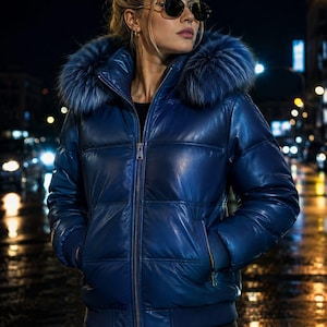 May include: A shiny blue puffer jacket featuring a high collar, a front zipper closure, and a large hood trimmed with thick, matching blue faux fur. The jacket has long sleeves with ribbed cuffs and two side pockets with visible zipper hardware.