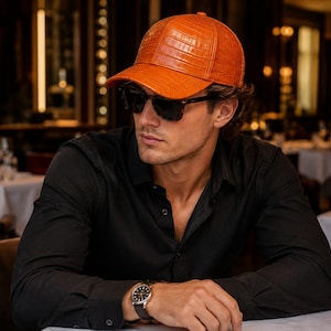 Puede incluir: Una gorra de béisbol de color naranja brillante con un patrón texturizado en relieve que imita la piel de cocodrilo. La gorra presenta una corona estructurada, una visera curva y un botón en la parte superior central.