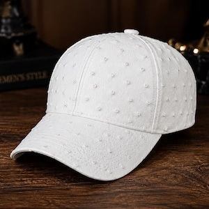 May include: A white baseball cap featuring a textured surface with small, raised circular bumps across the crown and the curved brim. The cap has a structured six-panel design with a small white button at the top centre and visible stitching.