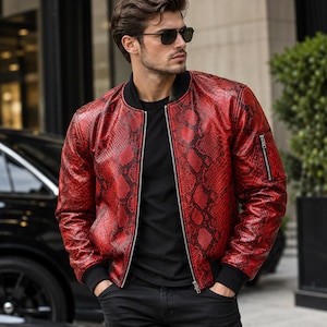 Puede incluir: Una chaqueta bomber roja y negra con estampado de piel de serpiente, cuello, puños y dobladillo de canalé negro. La chaqueta cuenta con una cremallera frontal plateada completa y un pequeño bolsillo utilitario con cremallera en la manga izquierda.