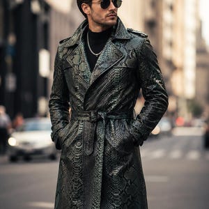 May include: A long trench coat featuring a dark green and black snakeskin pattern, a wide notched collar, shoulder epaulets, and a matching waist belt with a buckle. The coat is worn over a black turtleneck sweater with a silver chain necklace.