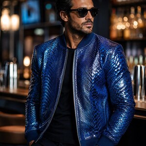 May include: A vibrant blue bomber jacket featuring a textured snakeskin-like pattern, a silver front zip, and dark blue ribbed cuffs and collar. The jacket is worn over a plain black t-shirt, paired with dark trousers and black sunglasses.