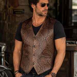May include: A brown and black snakeskin patterned vest featuring a V-neckline, four dark buttons down the front, and two horizontal welt pockets. The vest is worn over a plain black short-sleeved t-shirt and dark denim jeans.