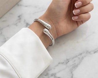 Piękna, masywna srebrna bransoletka typu bangle w designerskim stylu o nowoczesnym, rzeźbiarskim i wyrafinowanym designie, modnym organicznym kształcie fali z szykownym efektem lustrzanym.