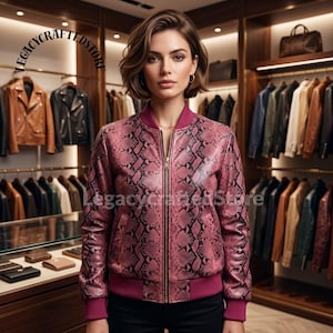 Puede incluir: Una chaqueta bomber rosa con estampado de piel de serpiente negra, con cuello, puños y dobladillo acanalados en un tono rosa oscuro sólido. La chaqueta tiene un cierre de cremallera metálico central y se muestra con el texto LEGACYCRAFTEDSTORE.