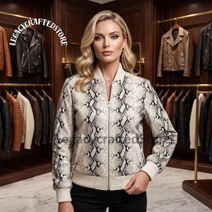 Peut inclure: Un blouson aviateur à manches longues avec un motif peau de serpent dans des tons crème, gris et noir. Le blouson possède une fermeture éclair frontale, un col, des poignets et un ourlet côtelés. Le texte LEGACYCRAFTEDSTORE est visible en haut à gauche.