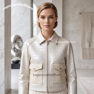 May include: A cream-coloured jacket featuring a glossy crocodile-embossed texture on the main body and sleeves, complemented by two front flap pockets with a distinct ostrich-skin pattern. The garment includes a pointed collar and a central zip.