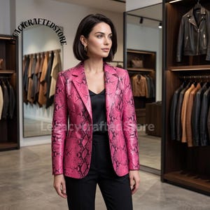 May include: A bright pink blazer featuring a black snakeskin pattern, a notched lapel, and two front pockets. The blazer is worn over a black camisole and black trousers. The text LEGACYCRAFTEDSTORE is visible in the upper left corner of the image.