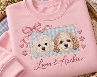 May include: A light pink crewneck sweatshirt featuring an embroidered rectangular patch with a blue and white gingham background. The patch displays two dogs, a pink ribbon, hearts, and paw prints. The text Luna & Archie is embroidered below.