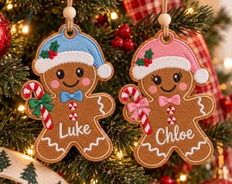 May include: Two embroidered gingerbread person ornaments hanging from twine with wooden beads. One wears a blue hat and bow tie with the name Luke, the other a pink hat and bow tie with the name Chloe. Both hold candy canes with holly.