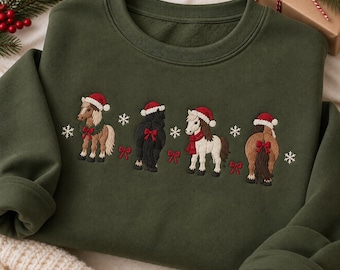 May include: An olive green crewneck sweatshirt featuring an embroidered design of four ponies wearing red Santa hats. The ponies are decorated with red bows, a green wreath, and a red scarf, interspersed with white embroidered snowflakes.