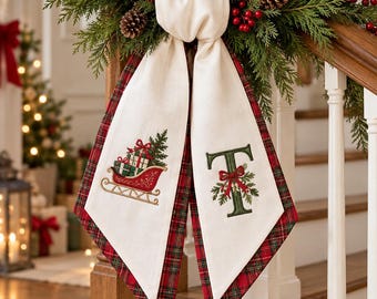 May include: A cream-colored fabric stair runner featuring a red sleigh with green gifts on one side and a large green letter T decorated with a red bow and holly on the other, finished with a red and green plaid border trim.