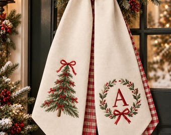 May include: A cream-colored fabric door hanger featuring two long, pointed tails. One tail displays an embroidered green Christmas tree with red bows, while the other features a green wreath with red berries and the red letter A.